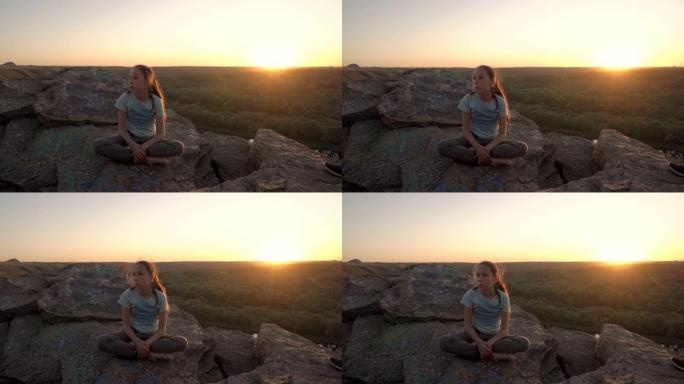 一个甜美沉思的少女坐在悬崖顶上，顶着黄色的夕阳。她的头发随风飘扬。日落时美丽的风景。肖像。4K。