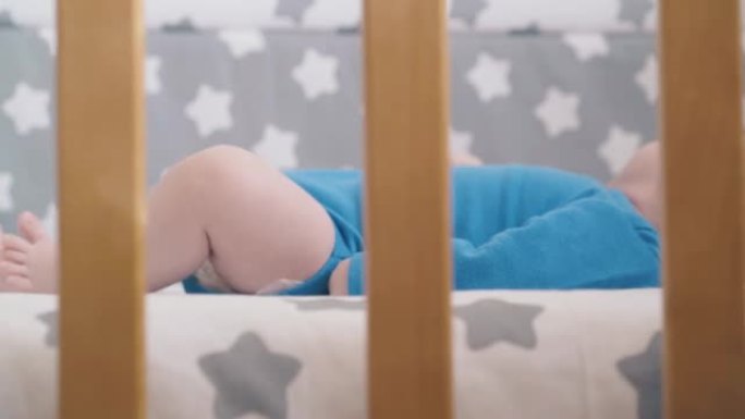 有趣的新生孩子困扰着躺在房间婴儿床上的手