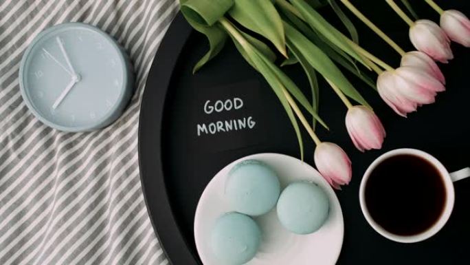 托盘上有法式马卡龙和新鲜郁金香，咖啡和闹钟的八点8点俯视图 “早上好”