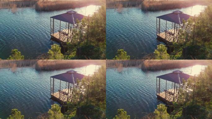 日落时河上有凉亭的小木码头。芦苇和冷杉之间的池塘上的空乔木，没有人。放松的地方，美丽的水景。