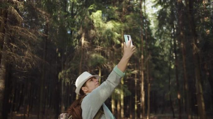 戴着帽子的旅行者女人试图在森林里的手机上捕捉手机信号，但手机上没有信号