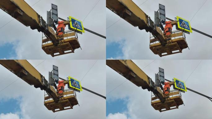 电梯托架中的一名工人在云层背景下修理LED交通灯。路标。LED技术。行人过路标志