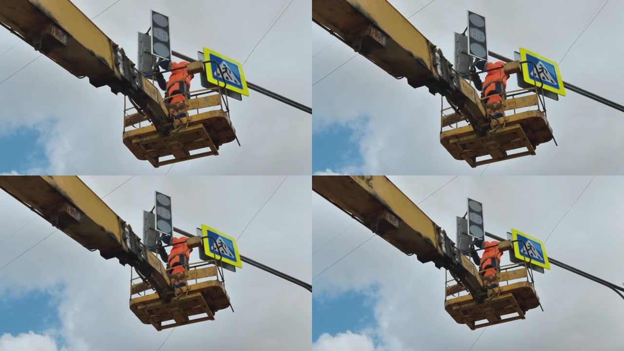电梯托架中的一名工人在云层背景下修理LED交通灯。路标。LED技术。行人过路标志