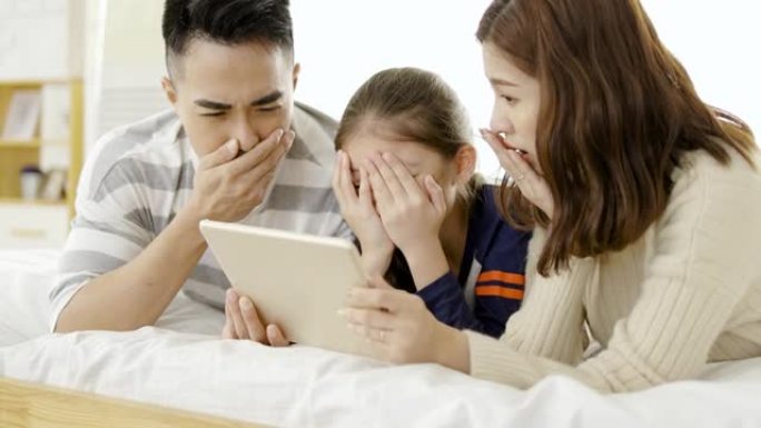亚洲家庭在床上用平板电脑观看恐怖电影