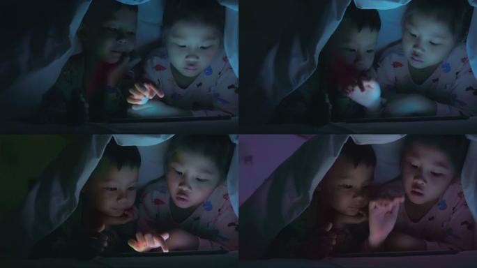 一个男孩和一个女孩晚上在毯子下使用平板电脑。