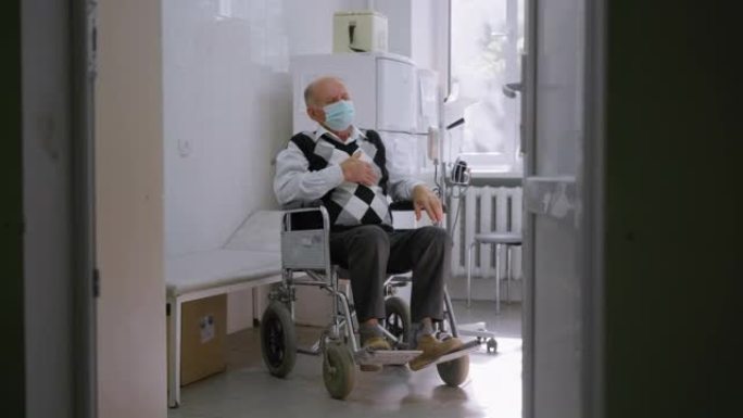 在医院内坐在轮椅上的保护性医用口罩上，老人在心脏疼痛时用手触摸胸部