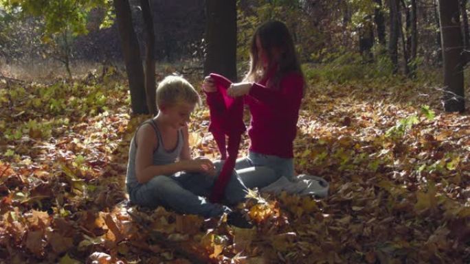 年轻的母亲在秋天的森林里给儿子换了毛衣