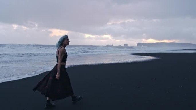 蓝色头发酷女孩沿着黑海滩散步