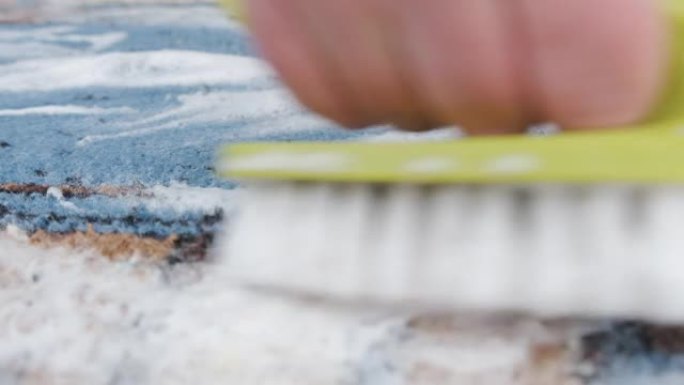 手工清洁地毯和地板覆盖物。一个人的手用刷子洗洗地毯织物。
