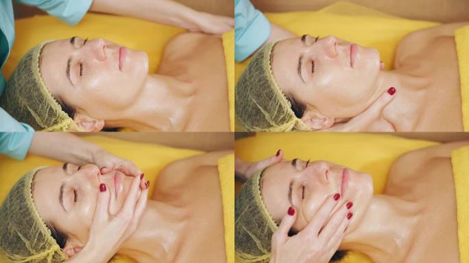 抗衰老美容。面部按摩。特写镜头，女人正在美容诊所接受面部和肩部按摩，以调理肌肉和面部皮肤淋巴引流。皮