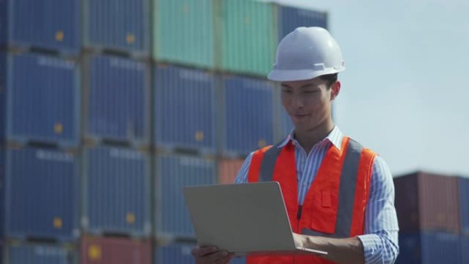 男性工人的肖像使用笔记本电脑控制从集装箱堆场的货物中装载集装箱箱。导入和导出概念。海运、承运和物流保