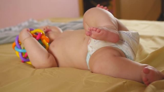 小宝贝躺在床上，用手握着玩具，轻咬一个玩具。儿童的感觉发育。特写镜头。