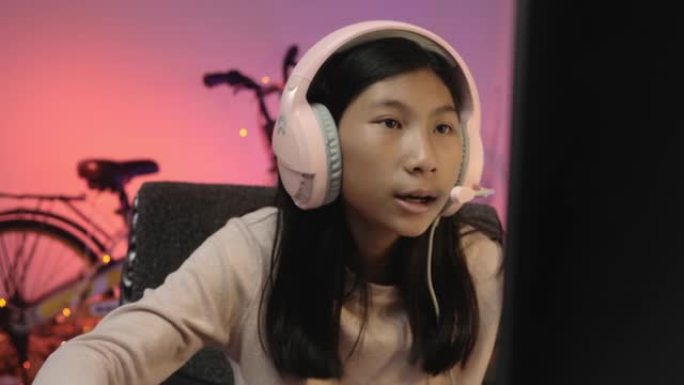 亚洲女孩使用耳机和电脑在家玩带发光二极管灯的在线游戏，一代阿尔法生活方式概念