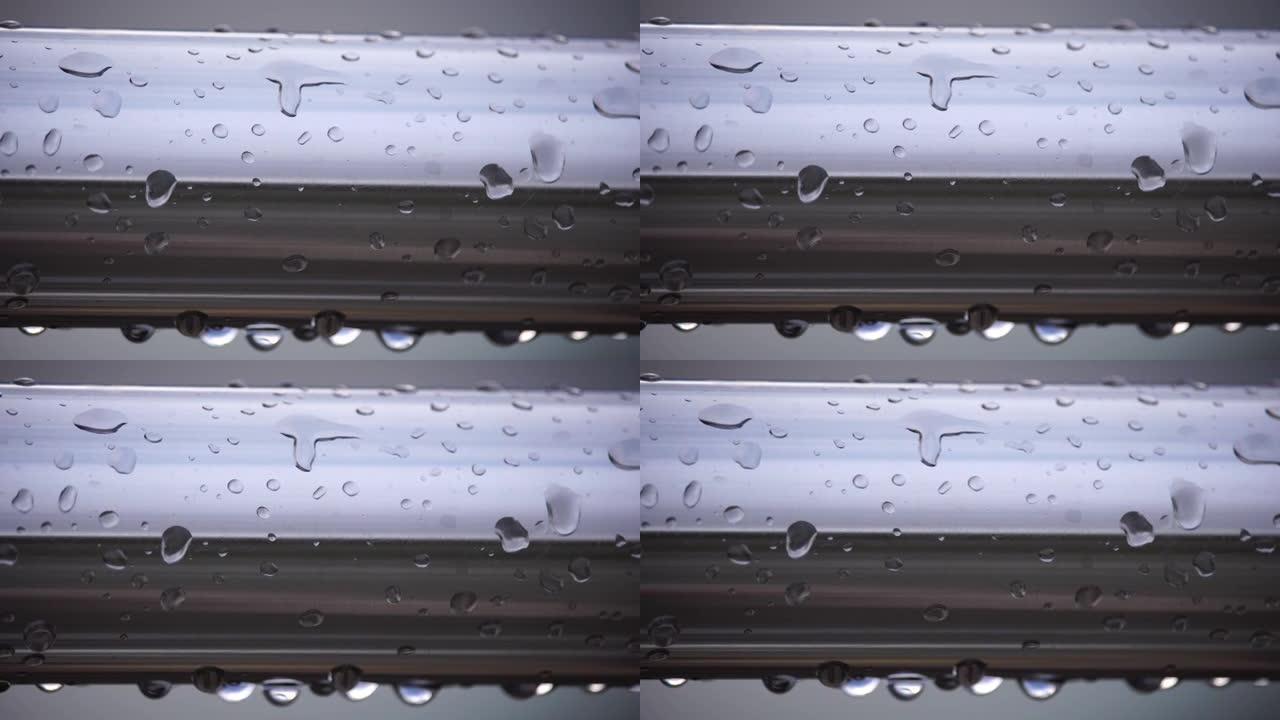 在模糊的海洋背景下，不锈钢扶手上的雨滴。特写镜头。雨露中的水滴聚集在闪亮的钢铬杆手轨栏杆上