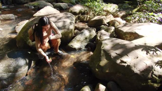 亚洲女性旅行者在热带森林中，有水流和落水的背景。自然旅行的概念。4k慢动作。