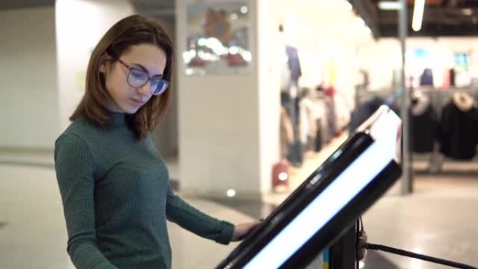 一名年轻女子正在购物中心的电子触摸台上观看导航地图。