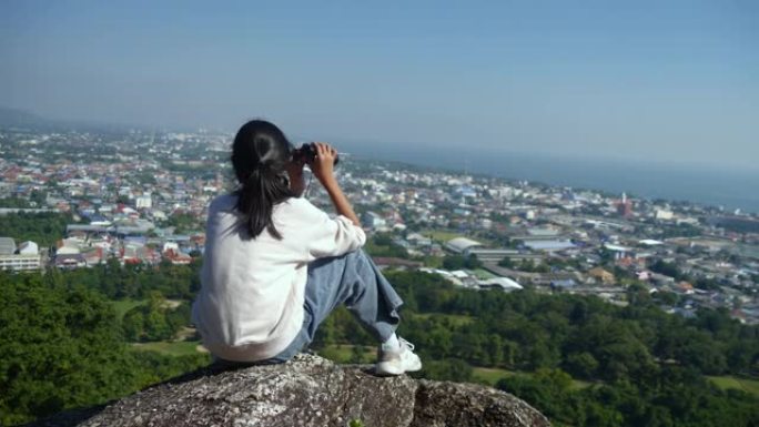 快乐的亚洲女孩用双筒望远镜在阳光明媚的日子里看着山顶的景色，生活方式的概念。