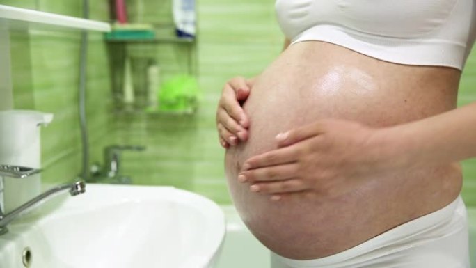 怀孕的女孩在浴室用奶油润滑胃以防止妊娠纹