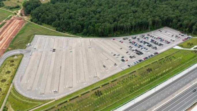 多车道高速公路和建筑高速公路附近有一个半空停车场。绿色的田野和周围的森林。路上交通轻松。上升无人机的