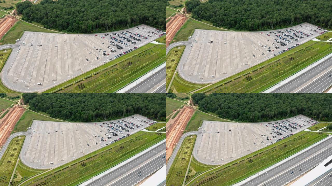 多车道高速公路和建筑高速公路附近有一个半空停车场。绿色的田野和周围的森林。路上交通轻松。上升无人机的