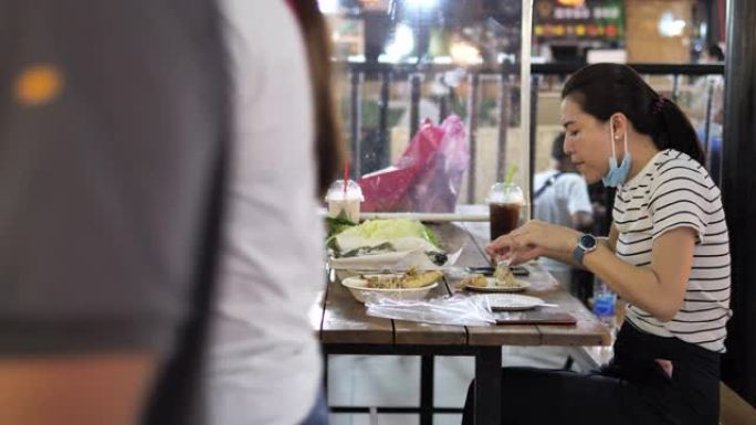 女人坐在餐厅分开吃食物，用桌子屏蔽塑料隔板保护冠状病毒新型冠状病毒肺炎的感染