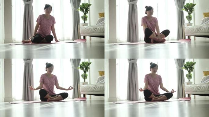 亚洲妇女在粉红色瑜伽垫上冥想，在早晨的阳光照射下，在家中健康的生活方式概念。