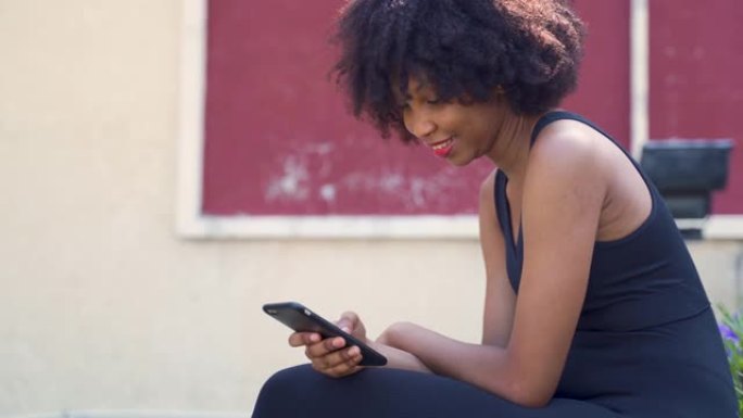 年轻的非洲裔美国妇女使用手机，坐在公园的长凳上。女性黑人慢跑者在户外休息和微笑