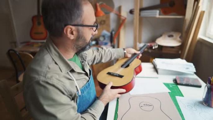 成熟的人在车间素描和制作新吉他