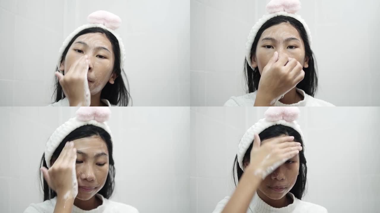 亚洲女孩早上在浴室用肥皂泡清洁她的脸，生活方式的概念。