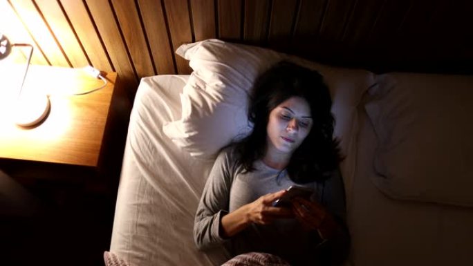 躺在床上的女人拿起手机并在睡觉前打开屏幕