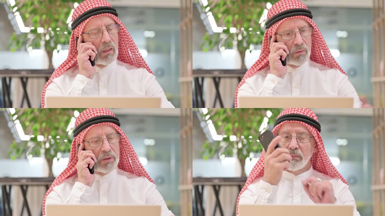 老阿拉伯商人，笔记本电脑在智能手机上聊天