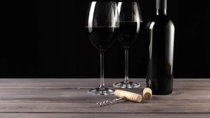 豪华红酒。两个酒杯，开瓶器，软木塞和一瓶红葡萄酒，由桌上的美味红葡萄制成，背景为黑色。慢动作。中枪。