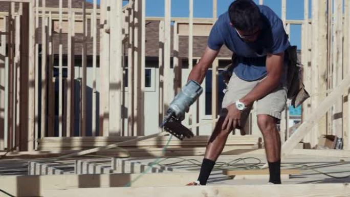 年轻的木匠建筑工人使用气动钉枪将木框墙放在一起，以在建筑工地上建造的住宅中垂直抬高