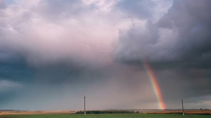 雨中充满戏剧性的天空，地平线上有彩虹。农业和天气预报概念。延时，延时，延时。秋季雨天的乡村草地