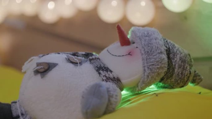 圣诞概念。闪烁着五颜六色的圣诞灯照亮了圣诞装饰。自制雪人躺在床上，面带微笑。
