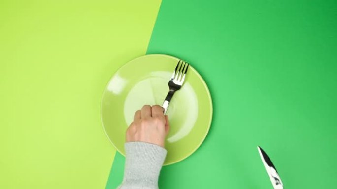 两只女性的手拿着一把金属刀叉，中间有一个空的圆形绿色盘子