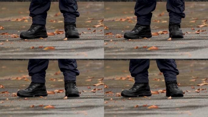 秋天。细节。他脚上穿的是军靴。警察的脚。穿制服的警官的靴子。一名执勤警察的腿靠近了。穿着黑色靴子的保