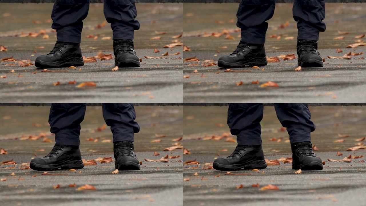 秋天。细节。他脚上穿的是军靴。警察的脚。穿制服的警官的靴子。一名执勤警察的腿靠近了。穿着黑色靴子的保