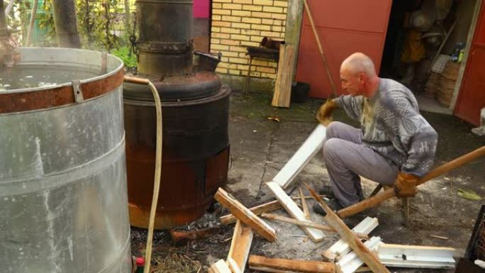 男子用斧头砍柴以在蒸馏设备下保持火势，他制作了家用酒精酒