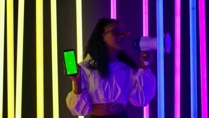 一位年轻可爱的女性非裔美国人的肖像在情感上向扬声器说了些什么，并显示了带有绿屏色度键的智能手机。促销