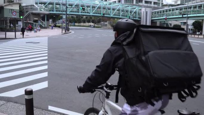 带着黑色背包的年轻人快递员在街上骑着自行车穿过城市，运送食物。过马路。送餐概念。
