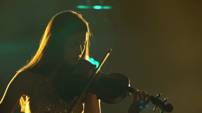 一个美丽的女孩在黑暗的工作室里拉小提琴的剪影，背景是动态的彩色霓虹灯。年轻漂亮的女人喜欢演奏乐器。特