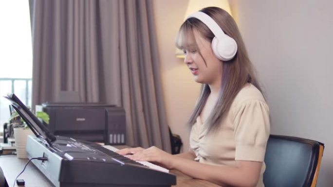 一个年轻的长发美丽的亚洲女孩少年正在她的房间日场景中用耳机练习钢琴键盘音乐。