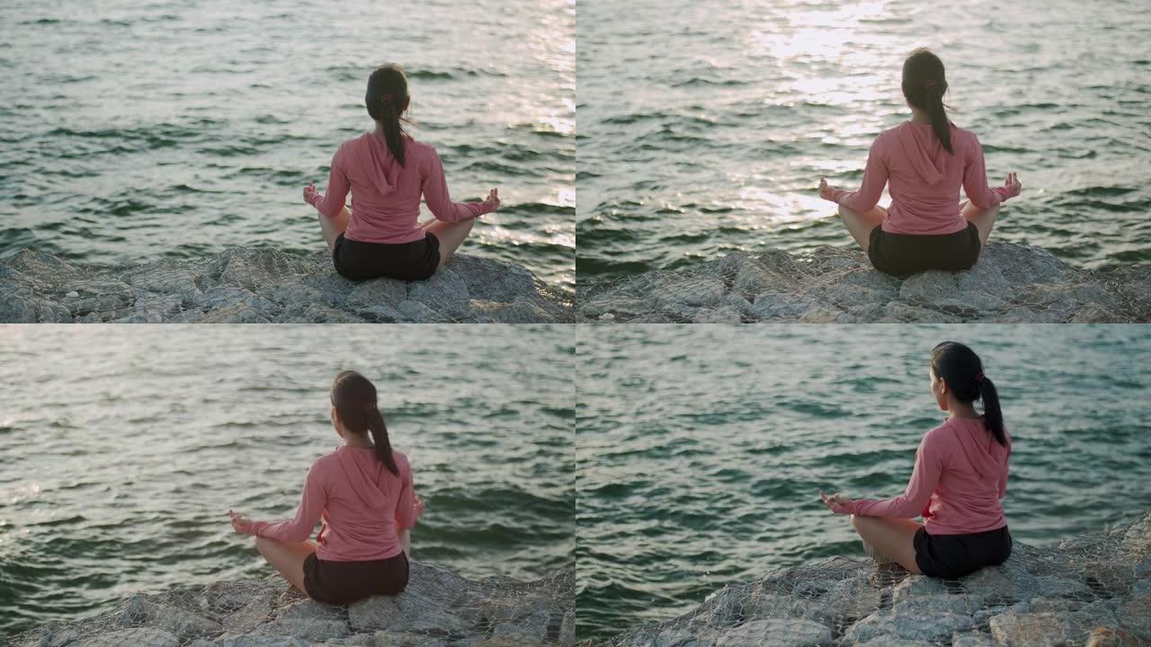年轻美丽的运动女孩训练冥想，日落时坐在石头海边。