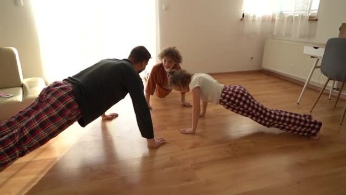 一个年轻的父亲训练他十几岁的孩子，一个男孩和一个女孩。穿着睡衣锻炼，有趣的视频，在锁定冠状病毒新型冠