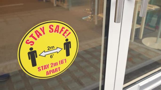 保持安全，间隔2m 6 ': 商店入口处门上的警告贴纸横幅。