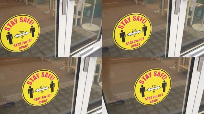 保持安全，间隔2m 6 ': 商店入口处门上的警告贴纸横幅。