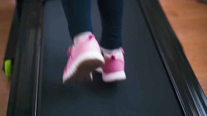 穿着粉红色运动鞋的活跃女孩在家里的运动员跑道上奔跑