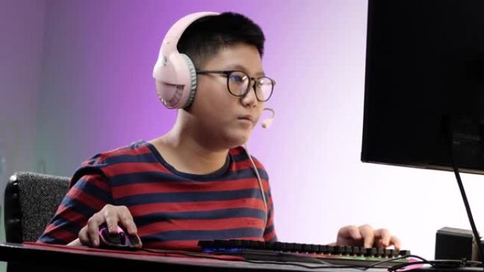 快乐的亚洲男孩在晚上在家玩网络游戏，带led灯背景，生活方式概念。