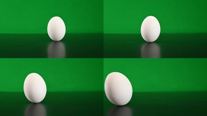 用手扭曲一个白色的鸡蛋，然后在chromakey背景上的深色硬表面上进行旋转。